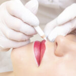 Young woman having permanent makeup on her lips at the beauticians salon. Permanent Makeup (Tattoo). drawing a contour with a white lip pencil